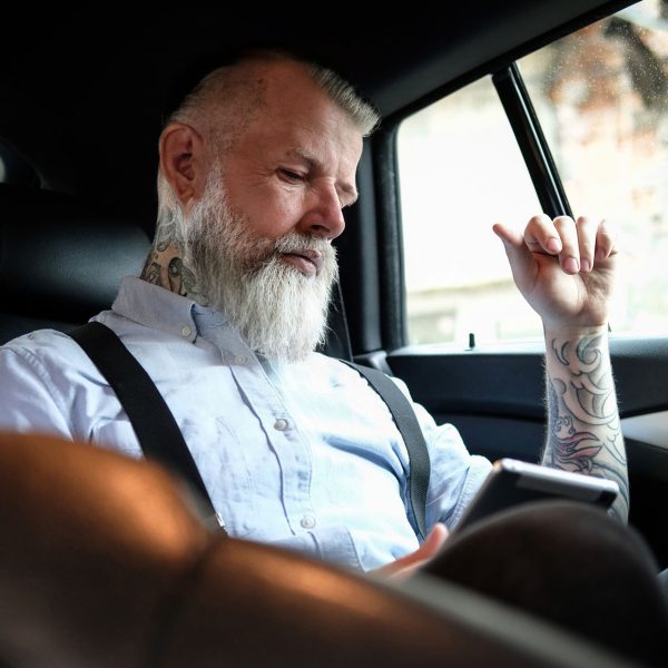 Shot of handsome elderly businessman dressed in stylish clothing with tablet inside car.